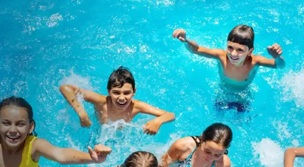 Niños riendo y chapoteando en una piscina azul, disfrutando del verano. ¡Una imagen perfecta de campamentos de inglés en España!