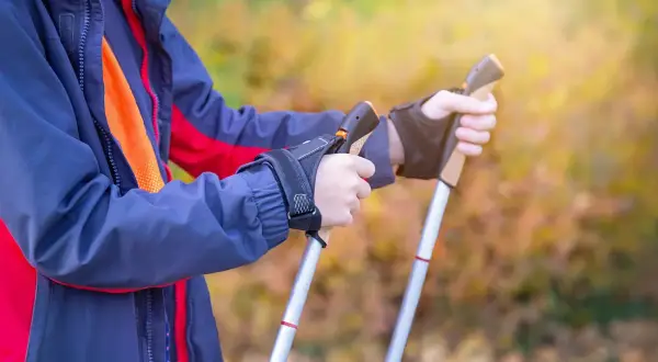 Osoba w kurtce przygotowuje się do marszu, trzymając kijki trekkingowe. Poznaj, jak chodzić z kijkami trekkingowymi, by czerpać z tego maksimum korzyści.