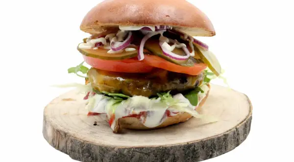 Soczysty burger z jalapeno, pomidorem, cebulą i ogórkiem na drewnianym plastrze.