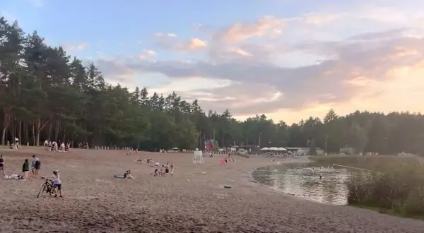 Plaża nad jeziorem w Jelczu-Laskowicach tętni życiem. Ludzie odpoczywają na piasku, kąpią się w wodzie, a dzieci bawią się przy dmuchanych zjeżdżalniach.