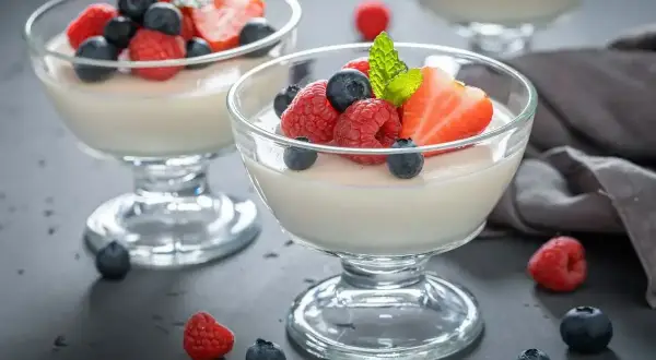 Två glas med krämig panna cotta, toppad med färska bär som jordgubbar, hallon och blåbär. En perfekt dessert.