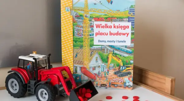 Czerwony traktor z ładowarką i rozsypanymi czerwonymi krążkami obok książki "Wielka księga placu budowy".