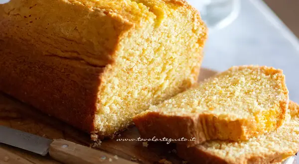 Plumcake senza yogurt dorato e soffice, tagliato a fette su un tagliere di legno con un coltello.