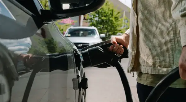 Persona che collega il cavo di ricarica a un'auto elettrica, un'azione che influisce sul costo ricarica auto elettrica.
