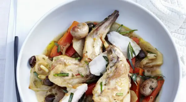 Ein köstliches Gericht mit zartem wirsing kaninchen, Karotten, Oliven und Kräutern in einer aromatischen Sauce, serviert in einer weißen Schüssel.