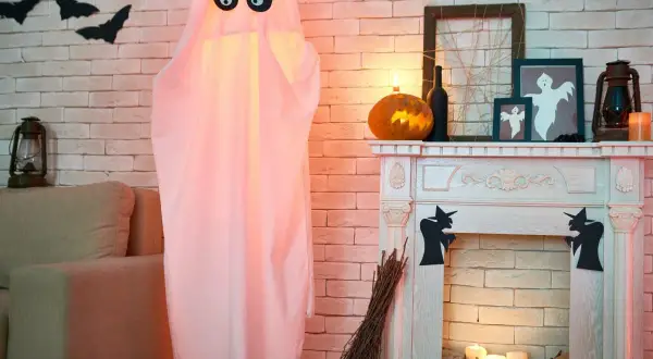 Duch z czarnymi oczami, dynia, kominek i nietoperze na ścianie - dekoracje na Halloween.