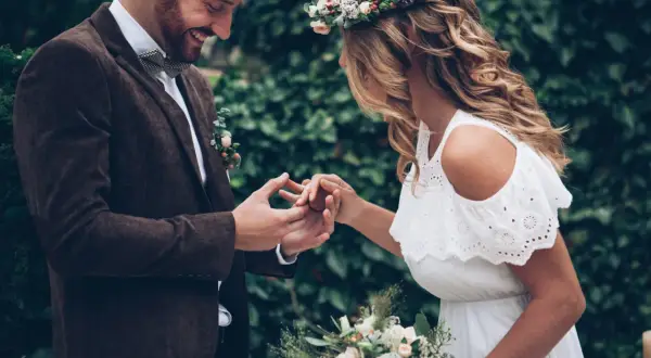 Para wesele w stylu boho: pan młody w brązowej marynarce i muszce, panna młoda w białej sukience i wianku.