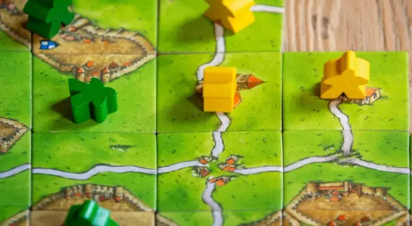 Zielone i żółte pionki na planszy z zamkami i drogami. Idealne dla fanów najlepszych gier planszowych.