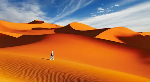 Un voyageur solitaire traverse la majestueuse dune du Sahara sous un ciel bleu éclatant.