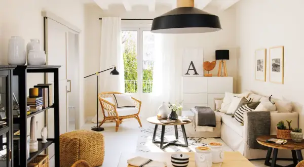 Salón luminoso con decoración de casas estilo nórdico moderno. Sofá beige, sillón de mimbre, mesa de centro redonda y estantería negra.