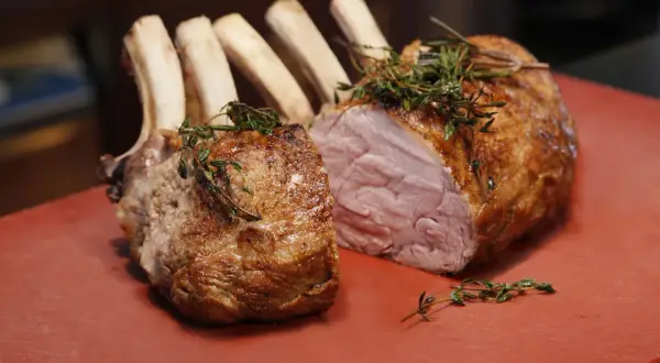 Ein saftiger Semerrolle Kalb Braten, mit Kräutern garniert, liegt auf einem roten Schneidebrett.