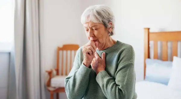 Ältere Frau hustet, kämpft mit Atemnot. Asthma kann zu einer Schwerbehinderung führen und den Alltag stark beeinträchtigen.