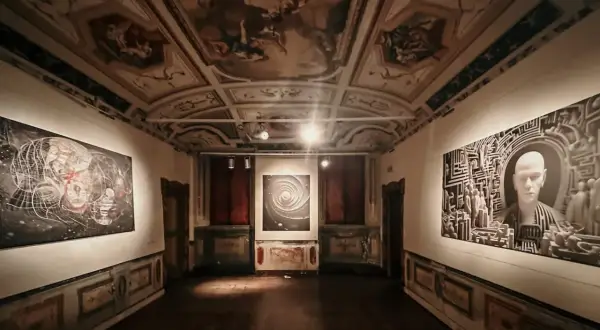 Sala di una galleria d'arte con soffitto affrescato e opere moderne. Le mostre ad Ancona presentano un'installazione con un volto stilizzato e un'opera astratta.