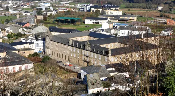 Vista aérea del monasterio de Mondoñedo, un imponente edificio de piedra con tejados oscuros, rodeado de casas y vegetación.