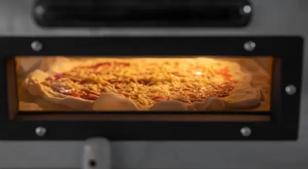 Ein Pizzateig, der 24 Stunden gereift ist, wird in einem Ofen gebacken. Er ist mit Tomatensauce und Käse belegt und verströmt einen köstlichen Duft.