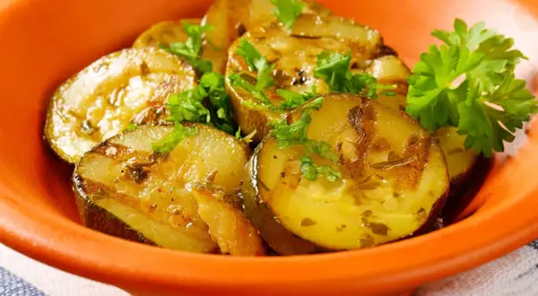 Gegrillte Schmorgurken mit Speck, garniert mit Petersilie, in einer orangen Schale.