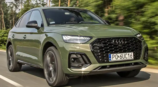 Zielony Audi Q5 Sportback w ruchu. Kierowca w okularach przeciwsłonecznych. Wiele pozytywnych audi q5 opinie o tym modelu.