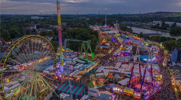 Buntes Lichtermeer auf Volksfesten im Herbst: Riesenrad, Hochbahn und Fahrgeschäfte beleuchten die Nacht.