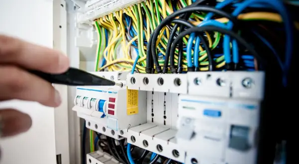 Ręka z narzędziem przy bezpiecznikach. Dowiedz się, jak znaleźć zwarcie w instalacji elektrycznej, analizując połączenia przewodów.