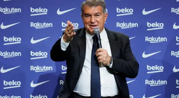 Joan Laporta, właściciel Barcelony, przemawia do mikrofonu na tle niebieskiej ściany z logo sponsorów klubu.