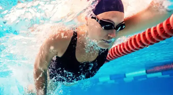 A swimmer in goggles and cap powers through the water. This image shows that boxers can swim, and do so with impressive strength and technique.