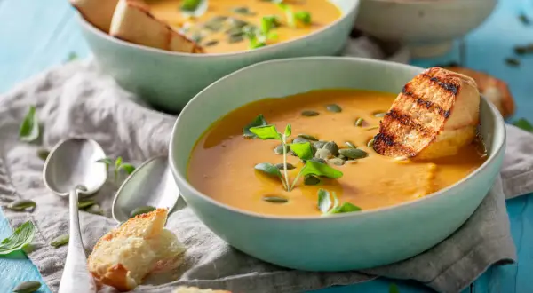 Zwei Schalen cremiger Kürbissuppe mit geröstetem Brot und Kürbiskernen. Perfekt für leichte Schonungskost-Rezepte.