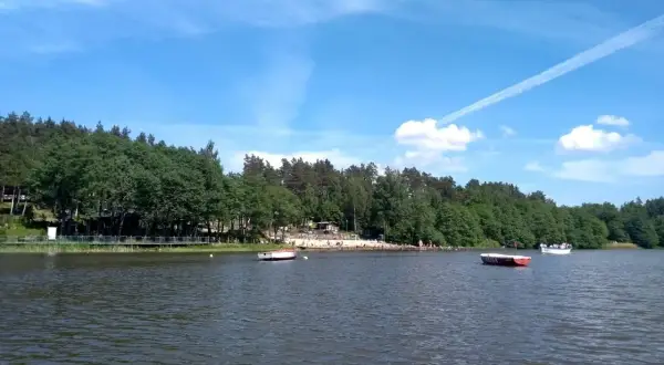 Spokojne jezioro Stobno otoczone zielonym lasem, z plażą i kilkoma łodziami.