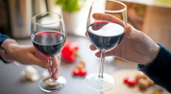 Dwie dłonie unoszą kieliszki z czerwonym winem, celebrując chwilę. Idealny sposób, jak pić wino.