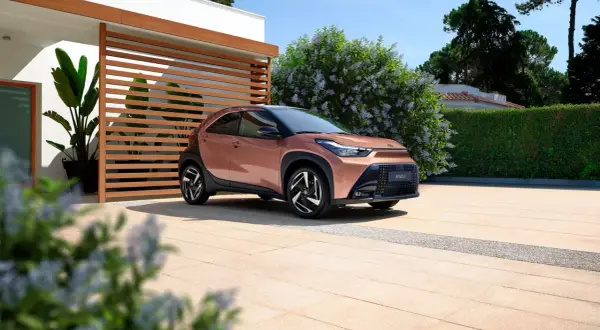 Różowy Toyota Aygo X na podjeździe przed nowoczesnym domem. Sprawdź atrakcyjną toyota aygo x cena!