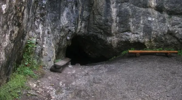 Wejście do jaskini w skale, obok ławka i kamienna ława. Tajemnicza dziura w górach, może w okolicach Zakopanego.