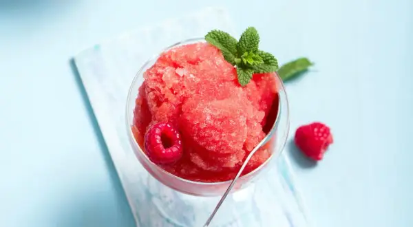 Erfrischendes Himbeer-Slush-Eis selber machen: Ein Glas gefüllt mit leuchtend rotem Slush-Eis, garniert mit frischen Himbeeren und Minze.