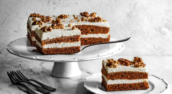 Pyszne ciasto marchewkowe z mascarpone, udekorowane orzechami włoskimi, prezentuje się apetycznie na białej paterze.