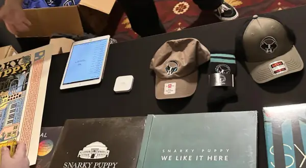 Snarky Puppy merchandise: vinyl records, hats, socks, and a tablet displaying a setlist.