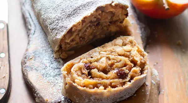 Strudel di mele con pasta sfoglia, cosparso di zucchero a velo, su tagliere di legno.