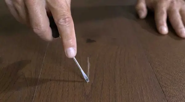 Mano che usa un cacciavite per sistemare parquet graffiato, un piccolo ritocco per un pavimento perfetto.