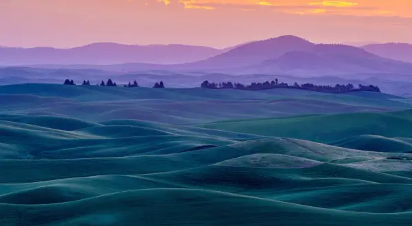 A fine art landscape photography captures rolling green hills under a vibrant sunset sky.