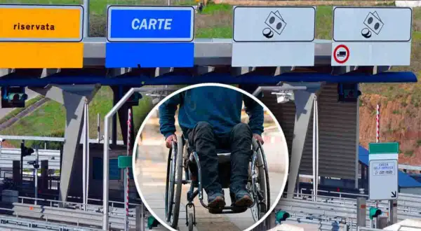Persona in carrozzina alla stazione di pedaggio autostradale, con segnali per corsie riservate e carte, per l'esenzione pedaggio autostradale invalidi.