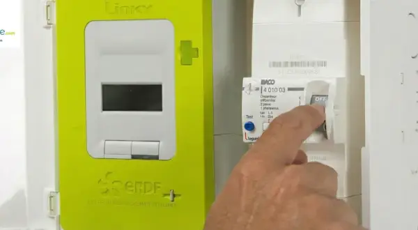 Main d'un homme actionnant un disjoncteur de type BACO en position OFF, à côté d'un compteur Linky vert.