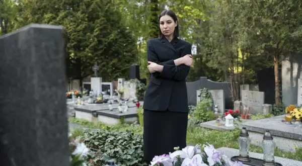 Smutna kobieta w czerni stoi na cmentarzu, otoczona nagrobkami. Jej postawa sugeruje częste chodzenie na cmentarz i głębokie przeżywanie żałoby.