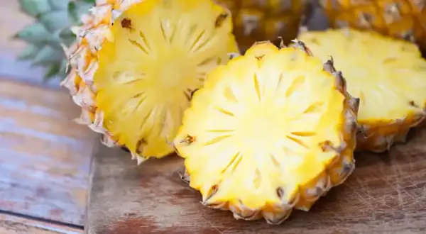 Dwa przekrojone ananasy na desce, jeden z nich wygląda jak ananas w ciąży, z widocznym wnętrzem i koroną.