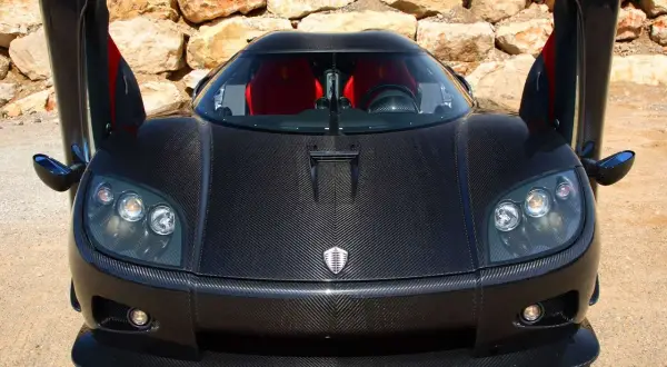 Czarny Pagani z otwartymi drzwiami, wykonany z włókna węglowego, z czerwonymi siedzeniami, na tle kamiennej ściany.