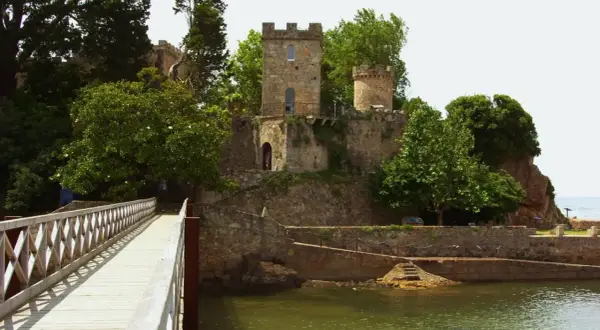 Un puente de madera conduce al histórico castillo de Santa Cruz, rodeado de exuberante vegetación y con vistas al mar.