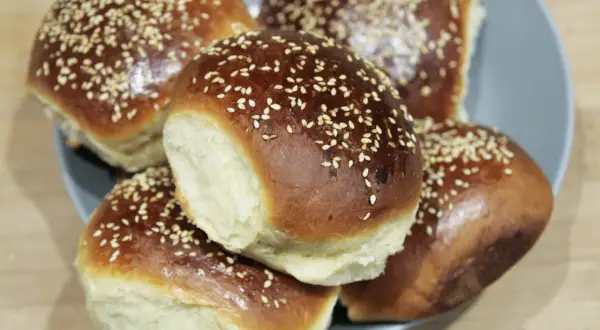 Pięć puszystych bułek do burgerów, posypanych sezamem, ułożonych na talerzu. Idealne na domowe burgery.