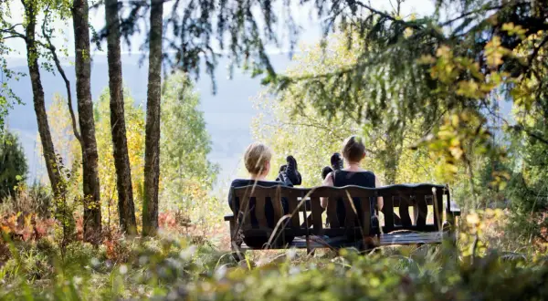 Två personer vilar på en bänk under en **weekend vandring i Sverige**. Höstfärger och solljus lyser upp skogen.