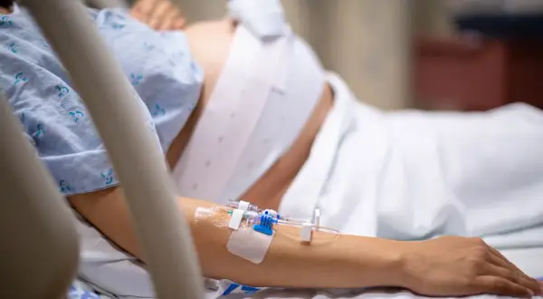 Kobieta w szpitalnym łóżku, z wenflonem w ręce, przechodzi trudny czas urlopu macierzyńskiego po poronieniu.