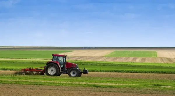 Tracteur rouge travaillant dans un champ, préparant le sol pour le semis direct. Paysage agricole sous un ciel bleu.