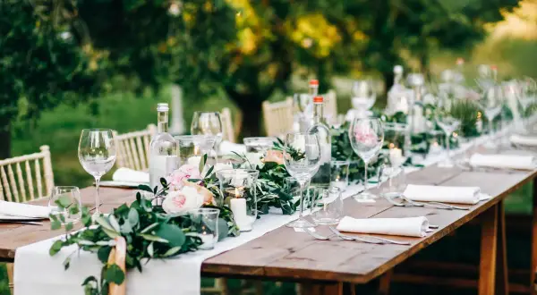 Tavola apparecchiata all'aperto con candele, fiori e bicchieri. Un esempio di addobbi tavoli matrimonio fai da te, con un tocco rustico ed elegante.