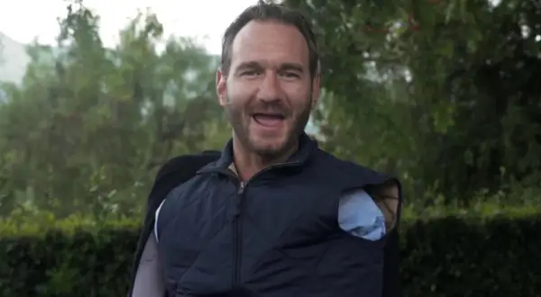 Nick Vujicic, lächelnd und mit offenem Mund, trägt eine blaue Weste über einem Hemd.