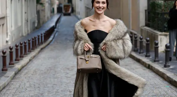 Elegante mujer con abrigo de pelo y bolso, lista para una boda en invierno.