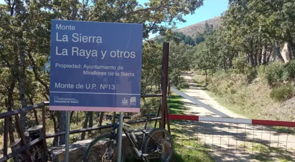 Señal de "Puerto de la Morcuera" junto a una bicicleta de montaña. Camino rural y árboles en un día soleado.